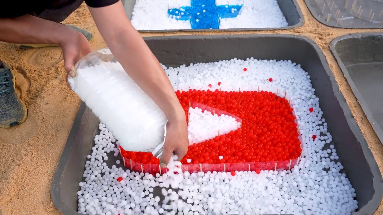 The four completed social media logos sit in their molds, surrounded by an array of colorful liquid-filled containers and materials on the sand.