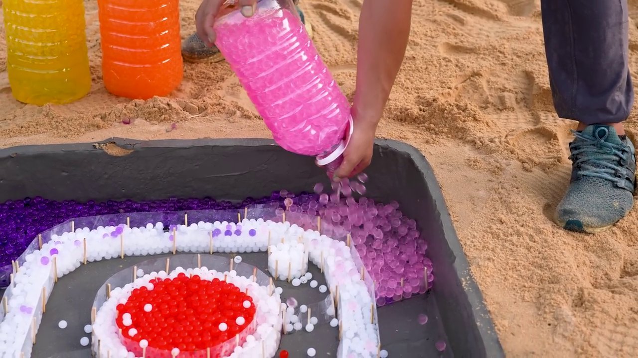 Colorful liquids are poured into a mold, creating a vibrant, foaming reaction that partially obscures the logo beneath.
